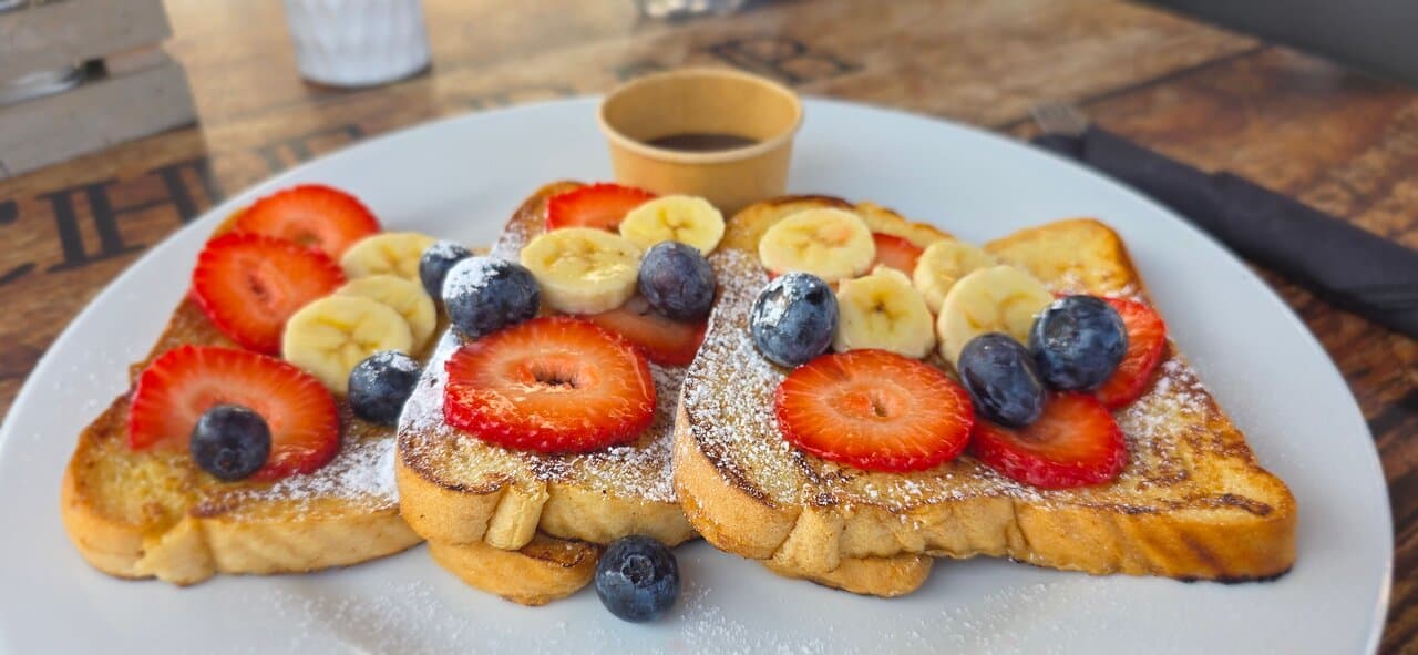 French Toast with fresh strawberries, blueberries and banana. Sprinkled with powdered sugar and served with syrup on the side.