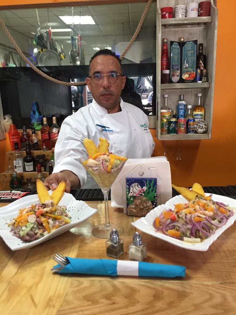 Our main chef, Orlando, holding ceviche platters with jumbo shrimp cocktail.