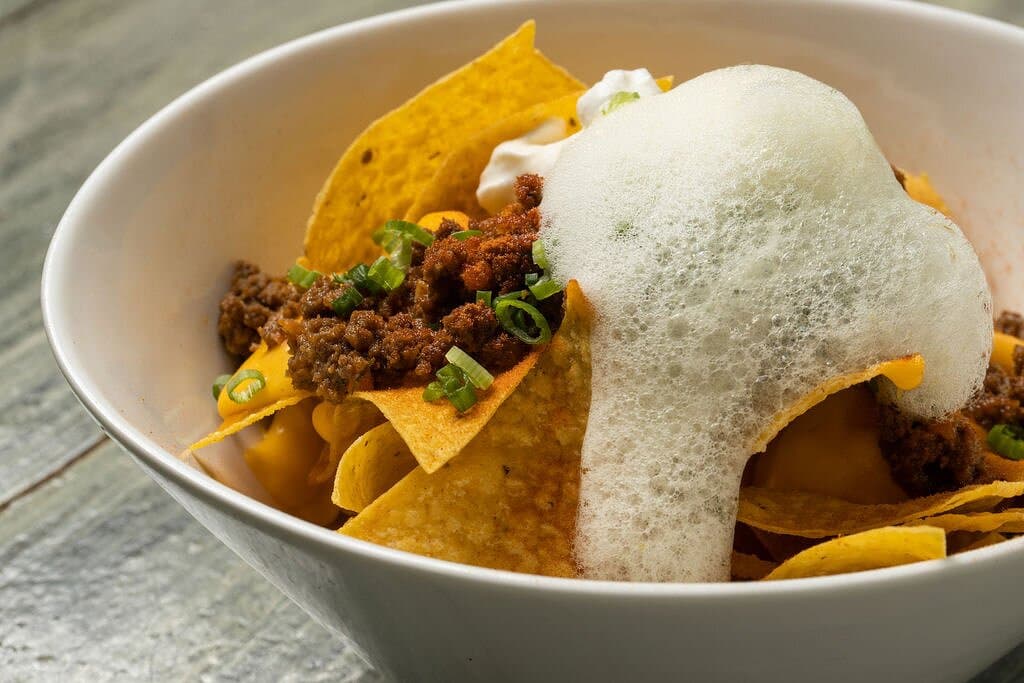 Macho nacho - crispy corn tortilla, melted cheese, ground beef ragu, scallions, tomato powder, jalapeño foam